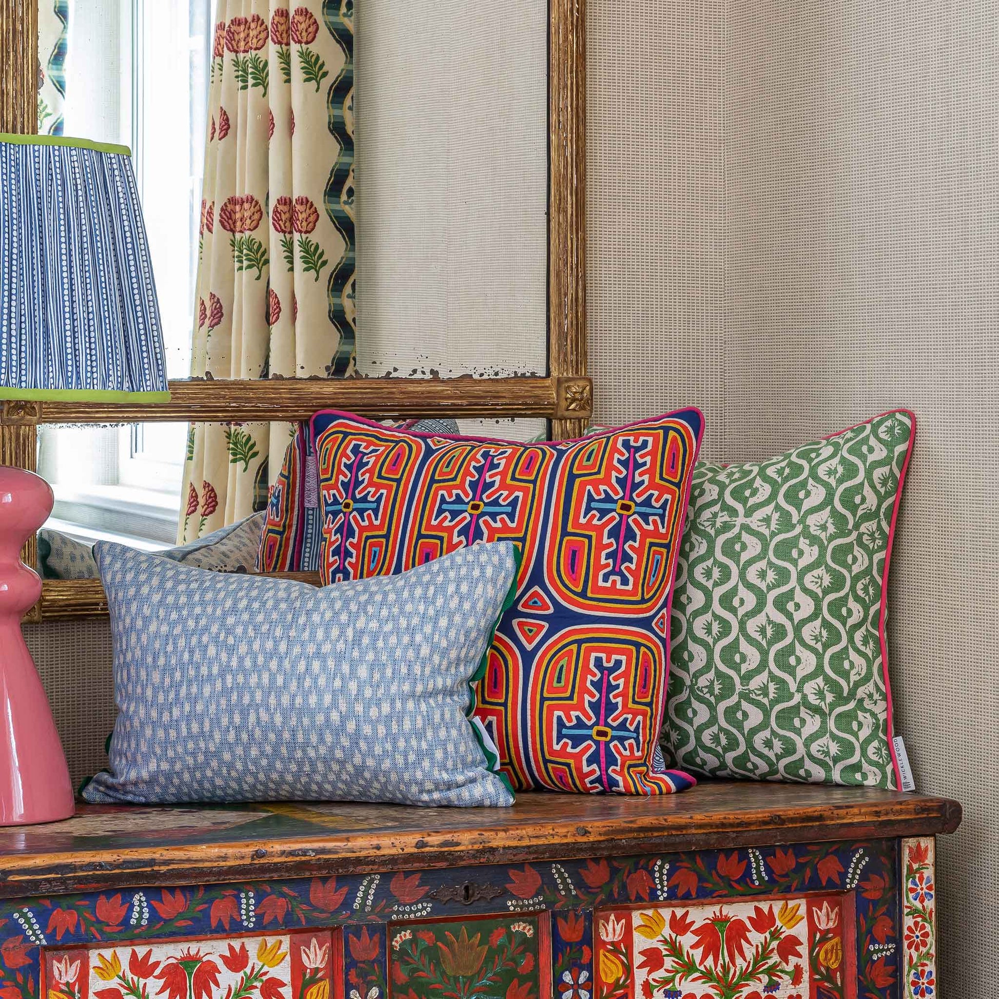 Geometric floral motif green square cushion with pink trim.